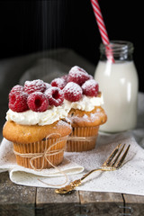 Muffins with soft cream and fresh raspberry powdered with sugar, bottle of milk with straw, rustic background