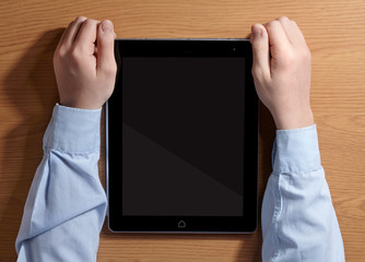 Boy holding a tablet PC sitting at the table. Top view.