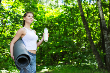 Young woman with a yoga mat outdoors.
