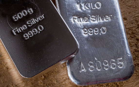 Two silver bullion on a background of a rough wooden texture. 1 kilo and 500 grams.