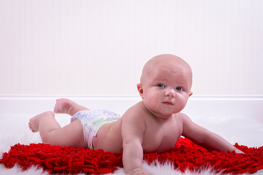 Adorable 6 month old baby boy laying down on a red heart blanket