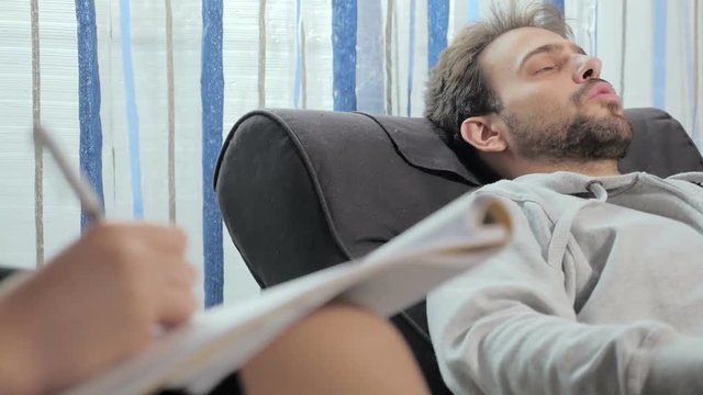 30 Year Old Man Lying On The Couch Talking To His Psychoanalyst Who Takes Notes