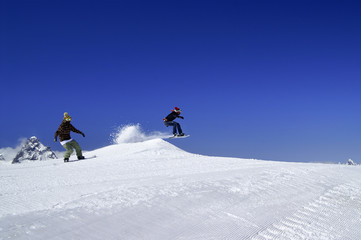 Naklejka na ściany i meble Two snowboarders jump in snow park at ski resort on sunny winter