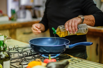 Chef in restaurant kitchen at stove with pan adding oil.