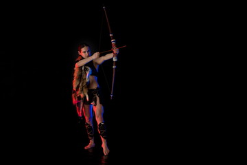 woman athlete in the Amazon costume with fur and skins posing on a black background in the scenic...