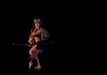 woman athlete in the Amazon costume posing on a black background in the scenic red and blue light.