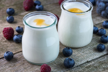 White yogurt with honey on the top in glass bowl on natural wood