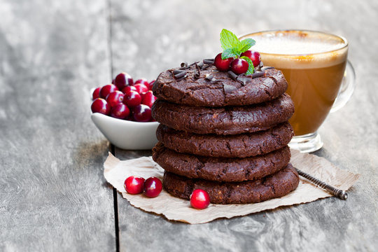 Stack  of dark chocolate cookies with cranberry and cup of coffe