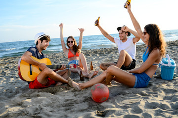 group of young people man and woman playing guitar singing having fun and party on beach at summer sunset holiday vacation