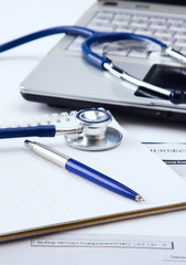 Stethoscope with clipboard and laptop on the desk