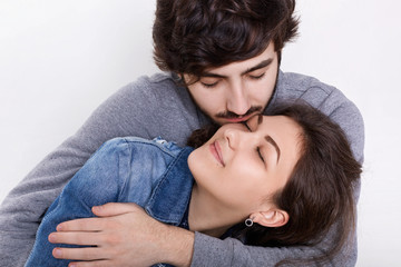 A loving couple isolated over white background. A young guy embracing and kissing his girlfriend. Sensual relationships between young people. Feelings, relations, romantic concept