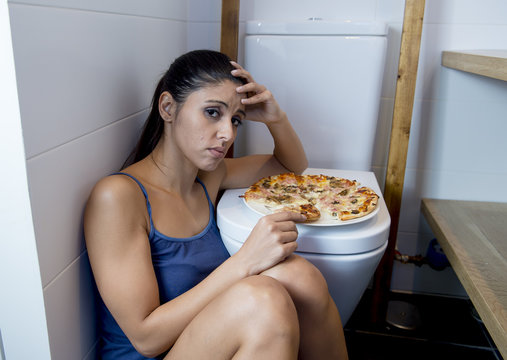 Bulimic Woman Feeling Sick Guilty Sitting At The Floor Of The Toilet Leaning On WC Eating Pizza