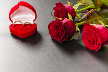 Beautiful red roses bouquet and wedding rings on a black background. Postcard for Valentine day or Wedding. Free space for text