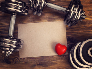 toned image of metal dumbbells and a red heart on a wooden background - 135981107