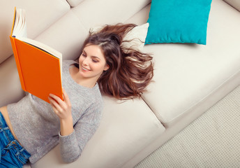 Girl reads a book lying at sofa
