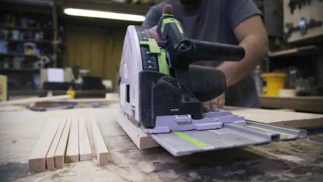 A craftsman is sawing a wooden bar using a power saw. Real time shot