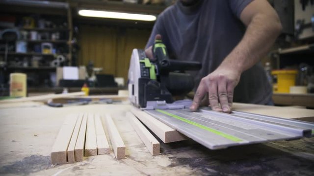 A craftsman is sawing a wooden bar using an industrial saw. Real time shot