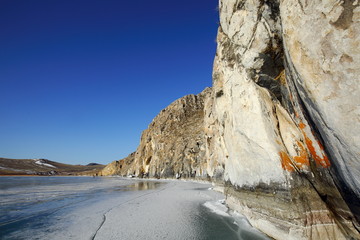 Fototapeta na wymiar Rocky headland on Rocky shore of lake Baikal in winter the Western coast of lake Baikal sticks in the ice-covered pond 