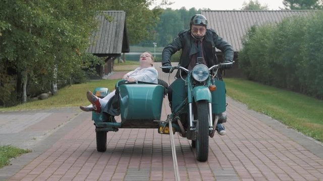 Biker with tie ride motorcycle with woman in nurse costume grimacing in sidecar