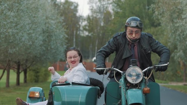 Biker ride in village motorcycle with woman wears nurse costume grimacing in sidecar