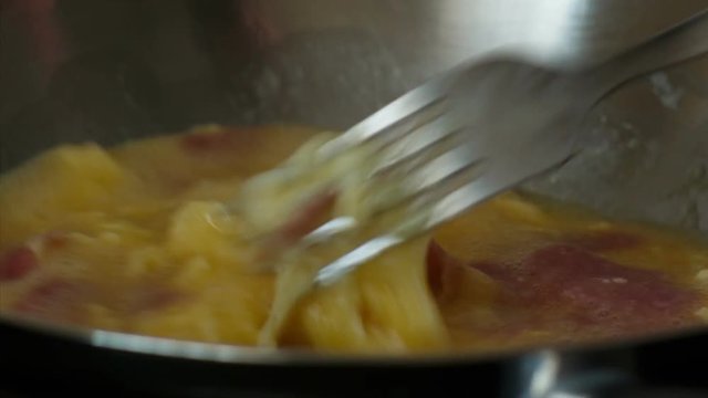 An authentic close-up food shot showing the preparation of scrambled eggs with bacon in a frying pan
