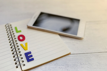 Valentine concept, colorful wooden love text over blank notebook with blurry smartphone, selective focus, vintage style