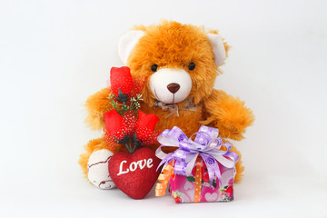 Brown teddy bear with a red rose and a gift box on a white background.