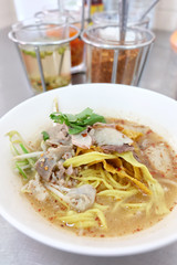 Bowl of Thai spicy noodles soup with pork and vegetables on table.