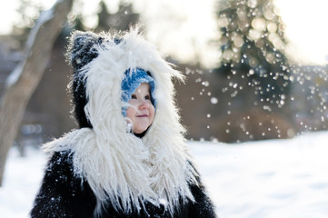 Little girl in fox fur coat looking at the falling snow in winte - 135997994