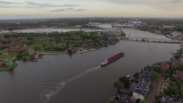 Aerial flight above the Koog Zaandijk, Netherlands. View of river, small countryside houses, dock, factory and fields