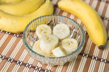A banch of bananas and a sliced banana in a pot over a wood background.