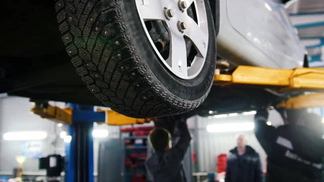 Car lifted in automobile service for repairing, workers fixing faults, slider