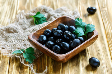 Black olives in a square wooden bowl.