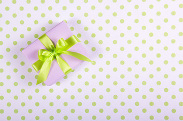 Lilac gift box with satin bow on a polka dot background. Copy space.