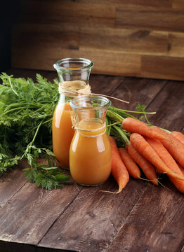 Fresh carrot juice in bottles and carrots on a grey wooden table