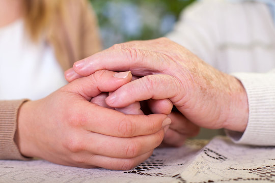 Elderly hands holding carer's hands