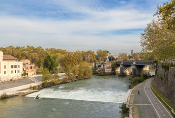 Fototapeta na wymiar Rome. Italy. Scenic view from the Pons Cestius: a dam on the river Tiber, the left - Isola Tiberina, the ruins of the ancient Emilio bridge and the current Ponte Palatino