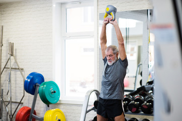 Fototapeta na wymiar Senior man in gym working out using kettlebells.