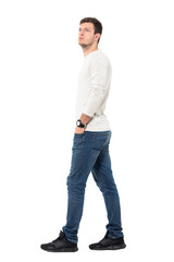 Side view of young relaxed casual man walking with hands in pockets looking up. Full body length portrait isolated over white studio background. 