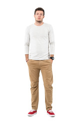 Serious young man in red sneakers and ocher pants with hands in pockets. Full body length portrait isolated over white studio background. 