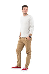 Naklejka premium Relaxed young man in beige pants and gray shirt smiling looking back over shoulder. Full body length portrait isolated over white studio background. 