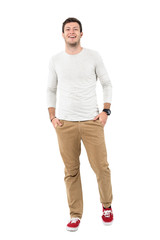 Fototapeta premium Cool young stylish man laughing with hands in pockets looking at camera. Full body length portrait isolated over white studio background. 