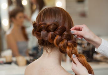 Beautiful, with long, red-haired hairy girl, hairdresser weaves a French braid, close-up in a...