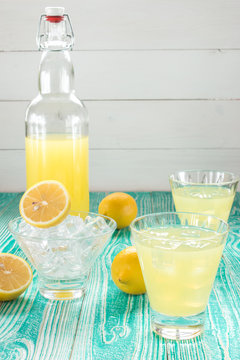 lemonade or limoncello in glasses with ice cubes, sherbet glass with ice cubes, lemon fruits on turquoise colored wooden table