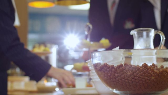 closeup bowl with chocolate cornflakes stands on table pupils takes cornflakes into plates with spoon in school canteen