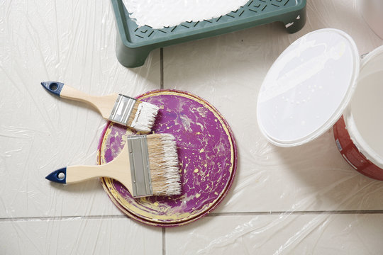 Brushes and cover of plastic bucket with paint on floor