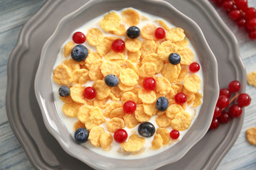 Tasty cornflakes with red currant and blueberries on gray wooden background