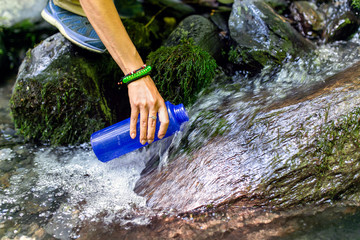 beautiful woman taking water from forest spring on hiking trip
