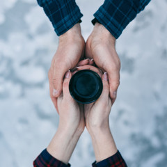 Top view of cup of hot tea in lover's hands against the background of a snow