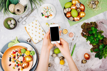 Workspace with easter decoration. Female hand holding a smartphone. Flat lay, top view